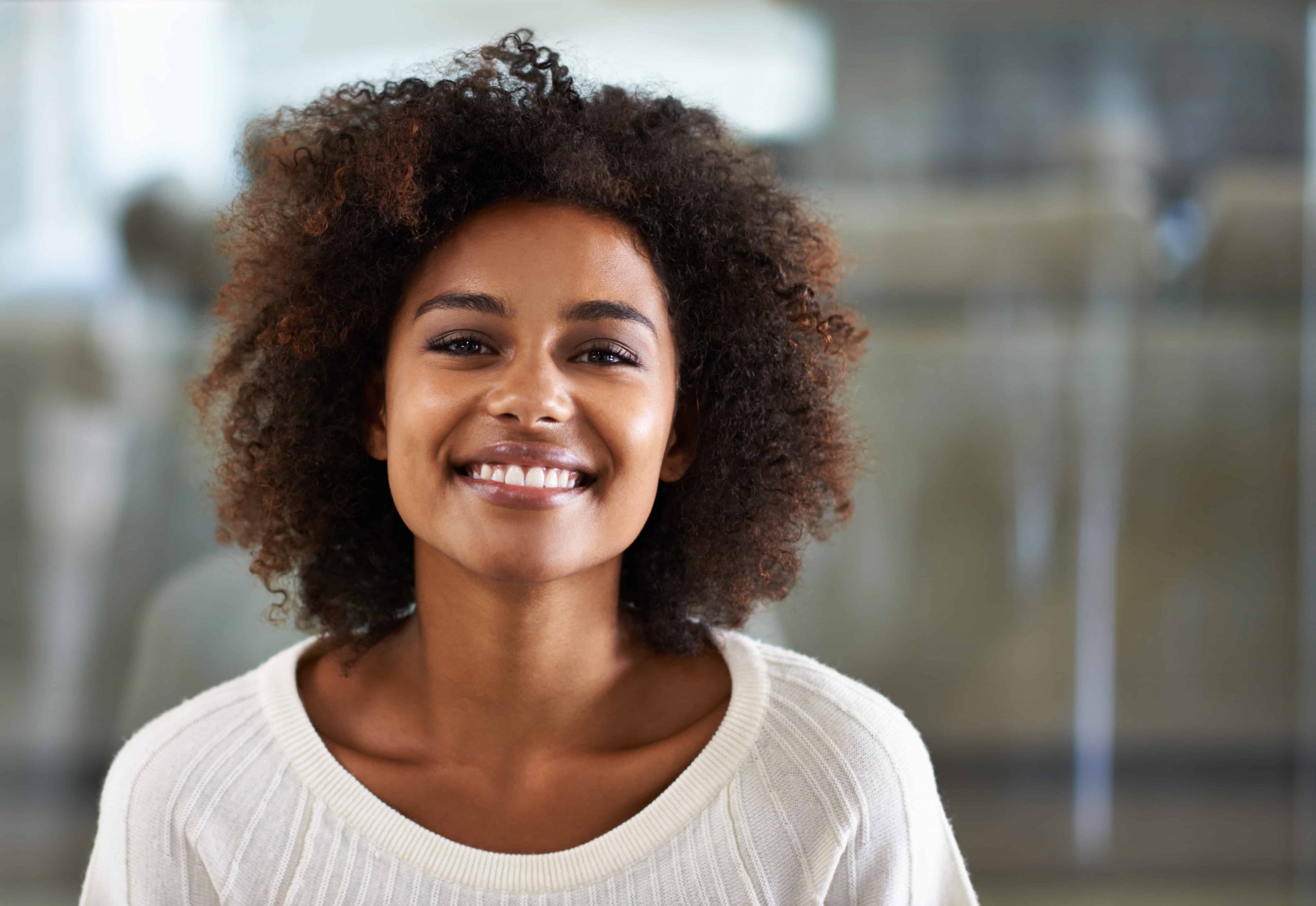 Femme souriante montrant un sourire éclatant après une chirurgie dentaire, dans un environnement lumineux et accueillant.